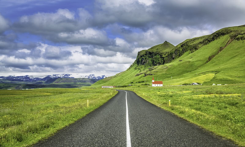 Icelandic highway with view of green fields and a mountain.